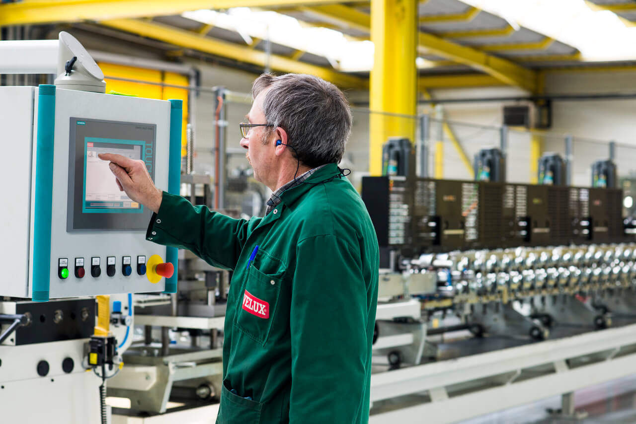 VELUX Angesteller bedient Kontrollpanel in industrieller Fabrikhalle mit Maschinen.
