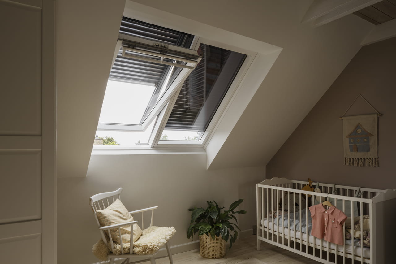 Mysigt vindrum för barn med VELUX takfönster, vit spjälsäng, gungstol och växt.