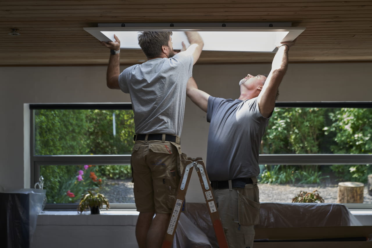 Dois homens a instalar uma janela de telhado VELUX, melhorando a luz natural do quarto.