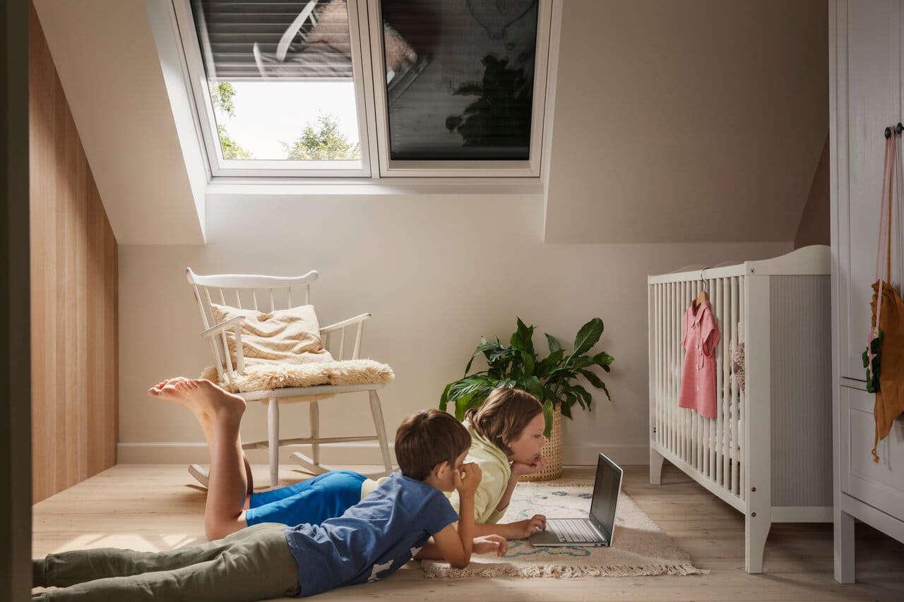 Kind op zolder speelkamer met VELUX raam, planten en laptop.