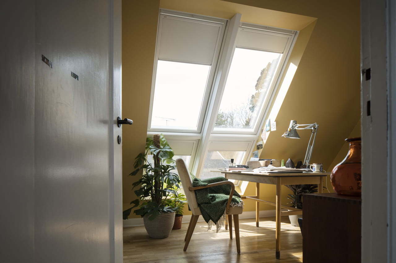Hyggeligt hjemmekontor med naturligt lys fra VELUX ovenlysvinduer, træ-skrivebord og planter.
