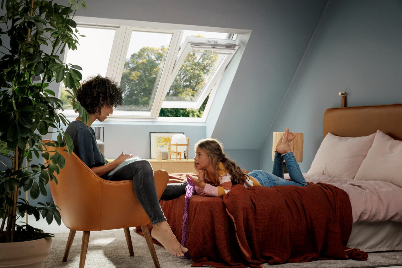 Camera da letto luminosa in mansarda con finestre per tetti VELUX aperte e un accogliente angolo lettura.