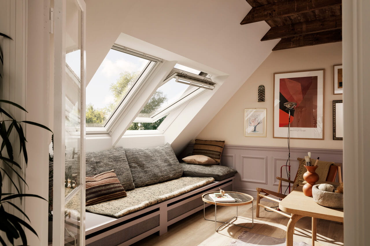 Sala de estar no sótão com janelas de telhado VELUX abertas e decoração elegante.