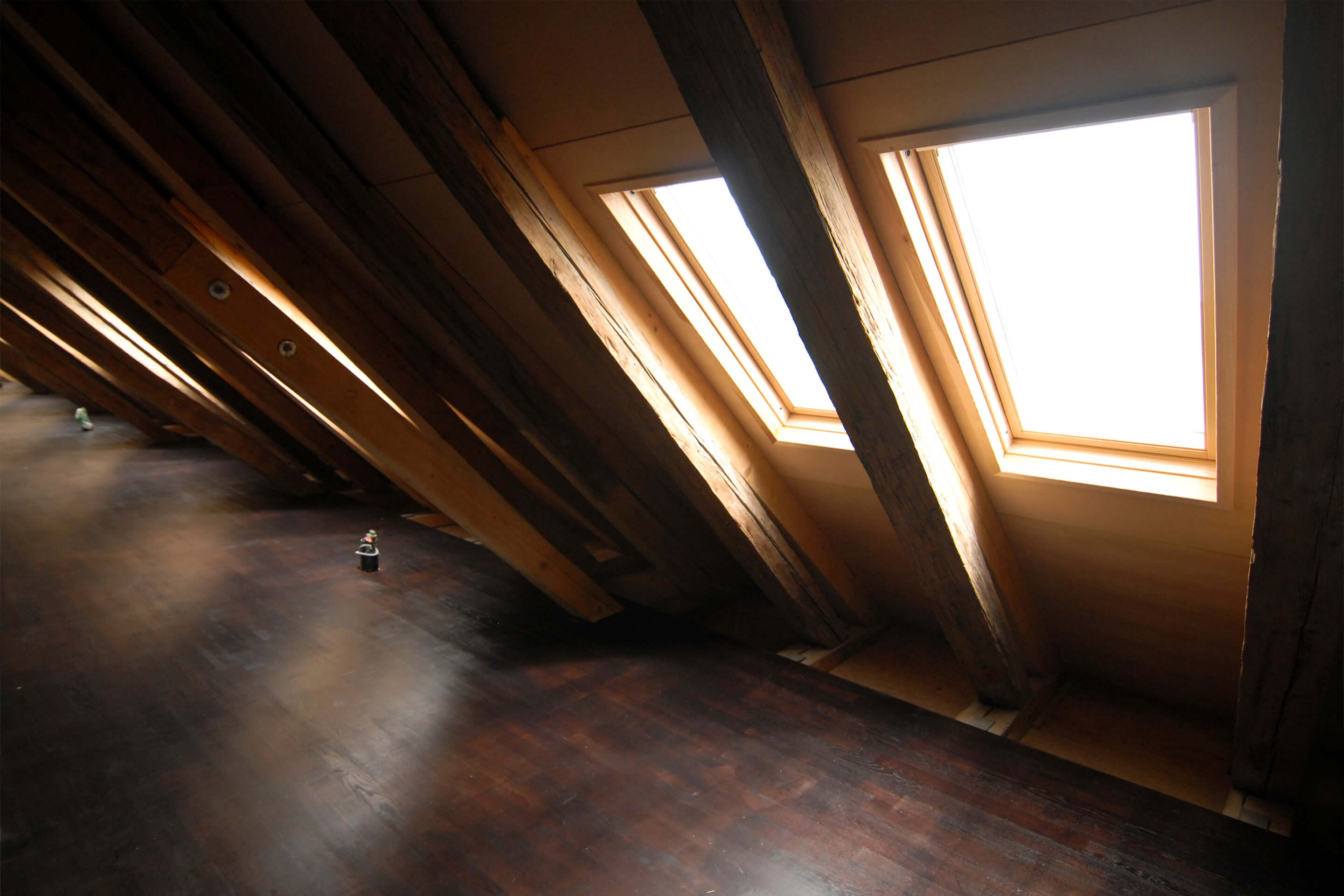 Sótão aconchegante com feixes rústicos e janelas de telhado VELUX permitindo a entrada de luz solar.