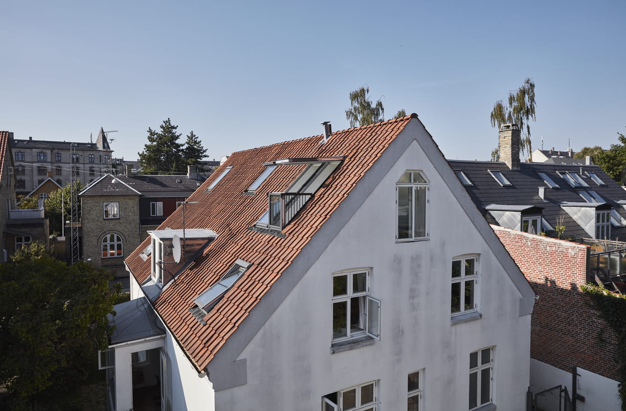 Bostadshus med röda takpannor och flera VELUX takfönster, omgivet av stadsgrönska.