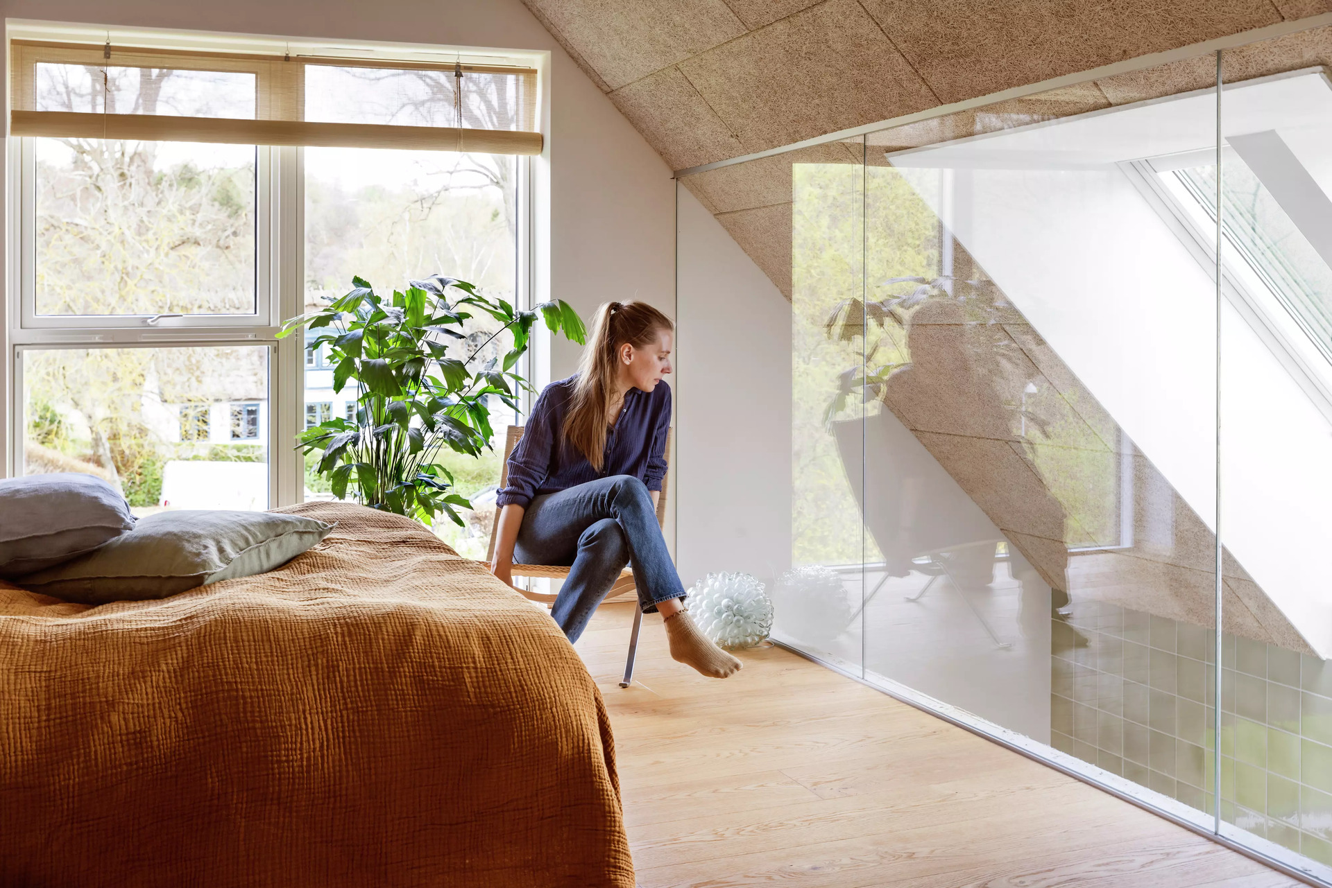 Koselig loftsoverom med VELUX takvindu og reflekterende glassvegg, med utsikt over grøntområder.