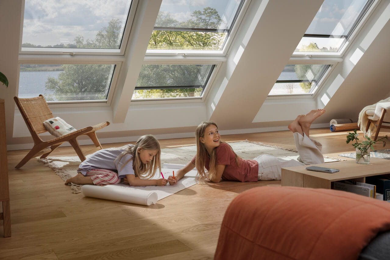 Kinderen in een zonovergoten zolder speelkamer met VELUX dakvensters met uitzicht op een meer.