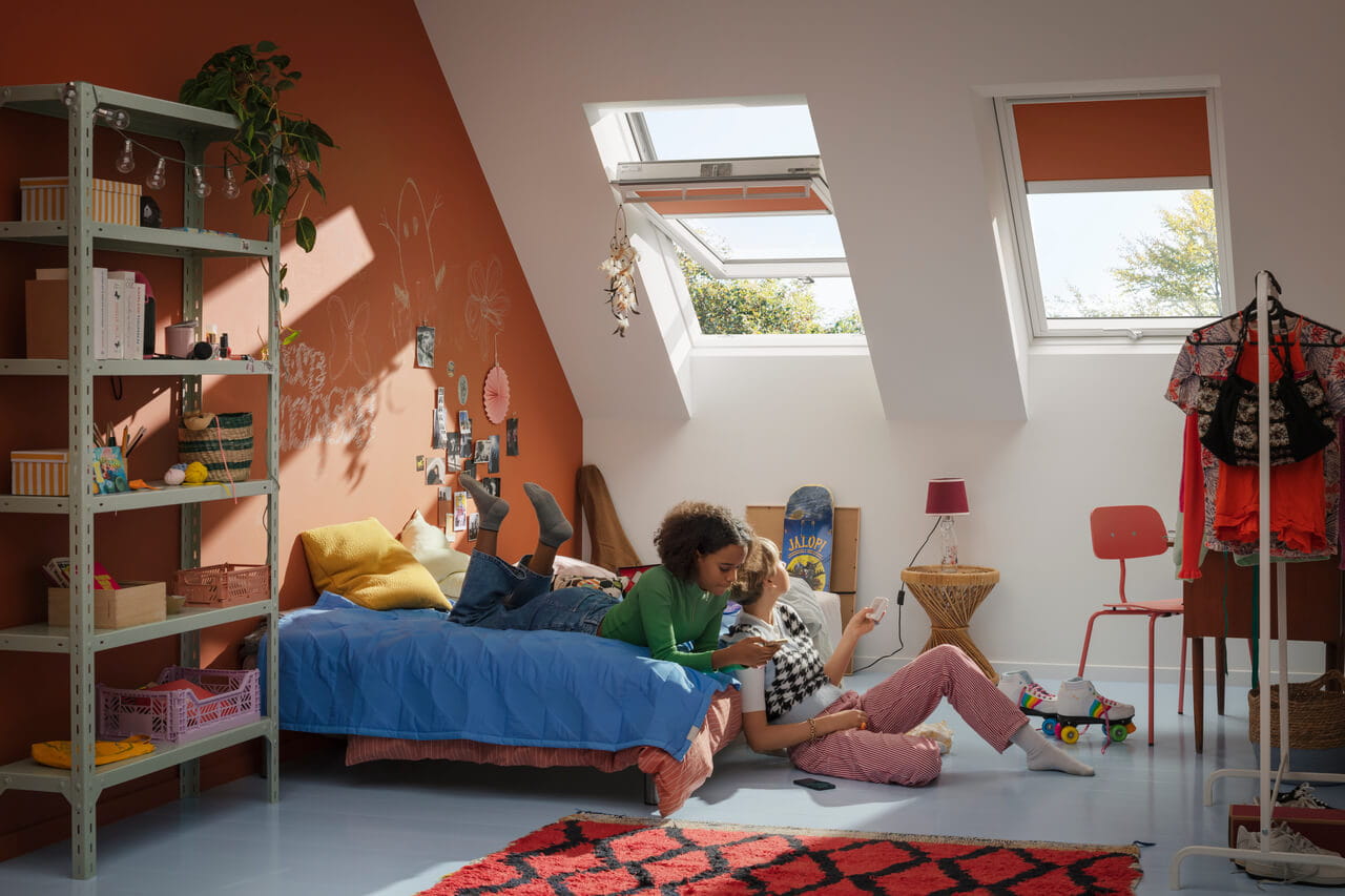 Chambre d'adolescent lumineuse avec une fenêtre de toit VELUX ouverte, des murs en terre cuite et une décoration personnelle.