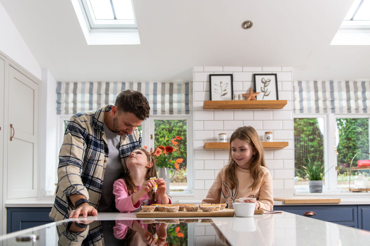 Bright kitchen with family baking, natural light from VELUX roof window, garden view.