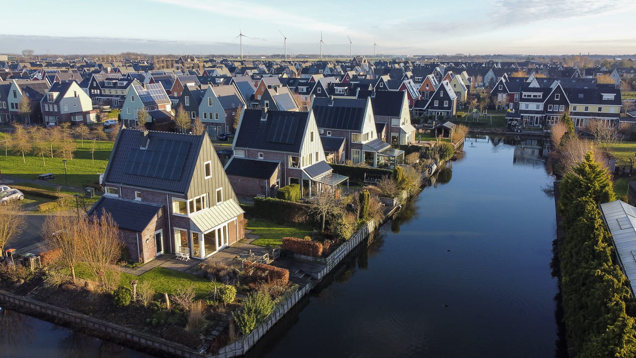 Luchtfoto van een buitenwijk met moderne huizen en solar panelen bij een kanaal.
