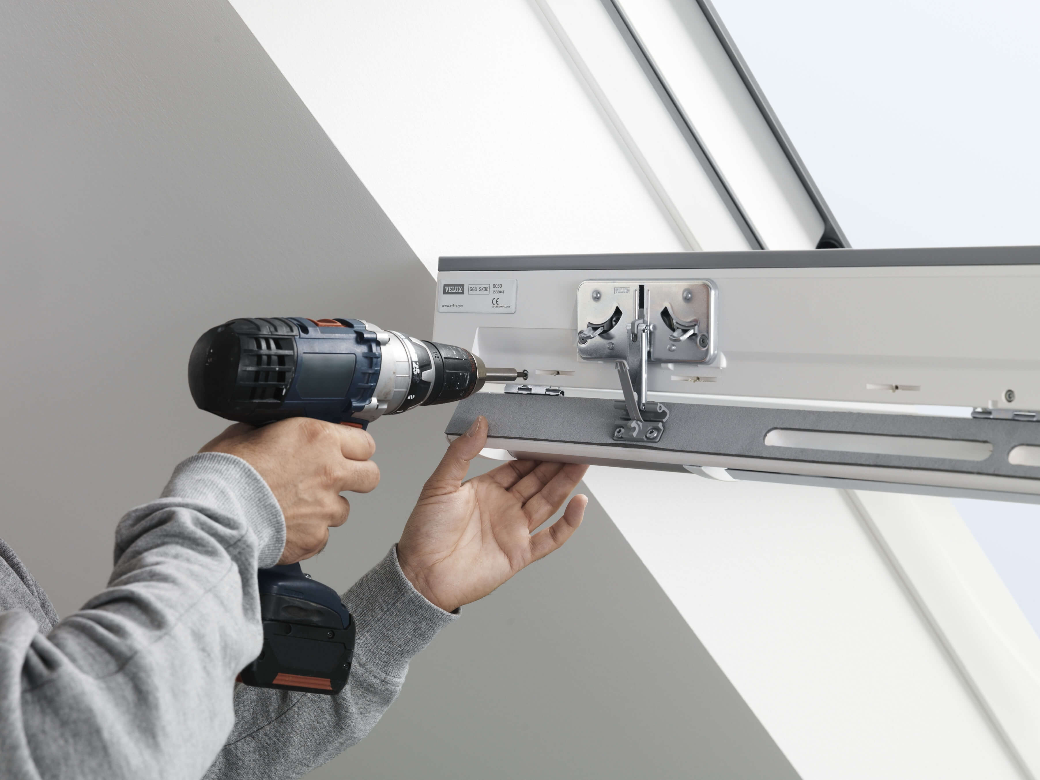 Nahaufnahme von Händen, die einen Bohrer verwenden, um einen VELUX Dachflächenfenster-Mechanismus zu installieren.