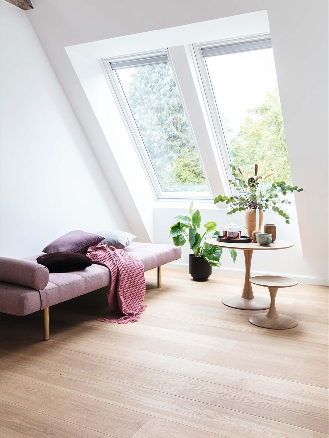 Wohnzimmer im Dachboden mit natürlichem Licht durch VELUX Dachflächenfenster, lila Sofa und Pflanzen.