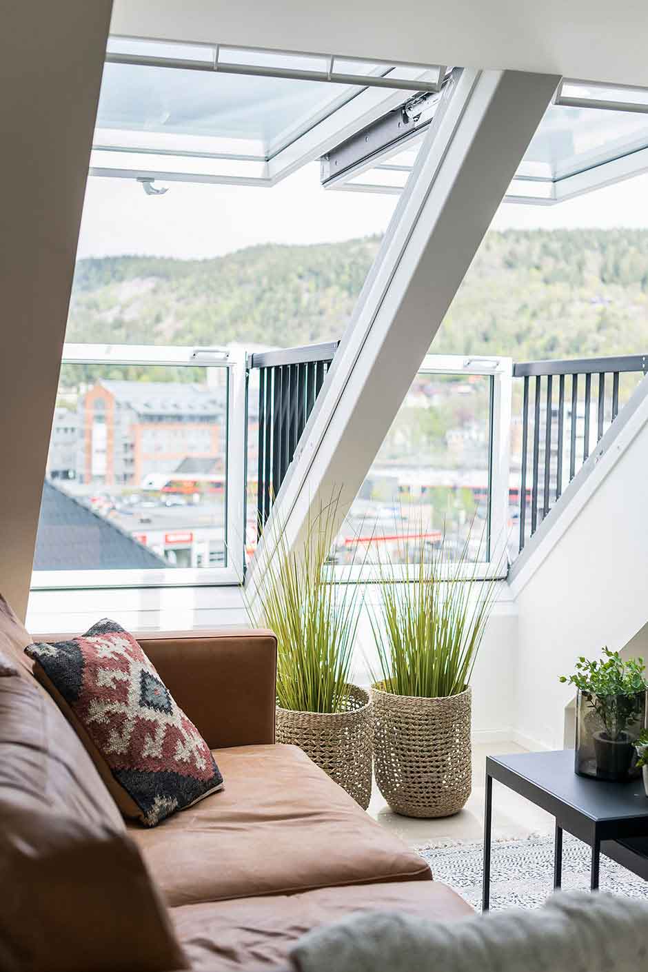 Modernes Loft mit VELUX Dachflächenfenster, Ledersofa, Pflanzen und städtischem Ausblick.