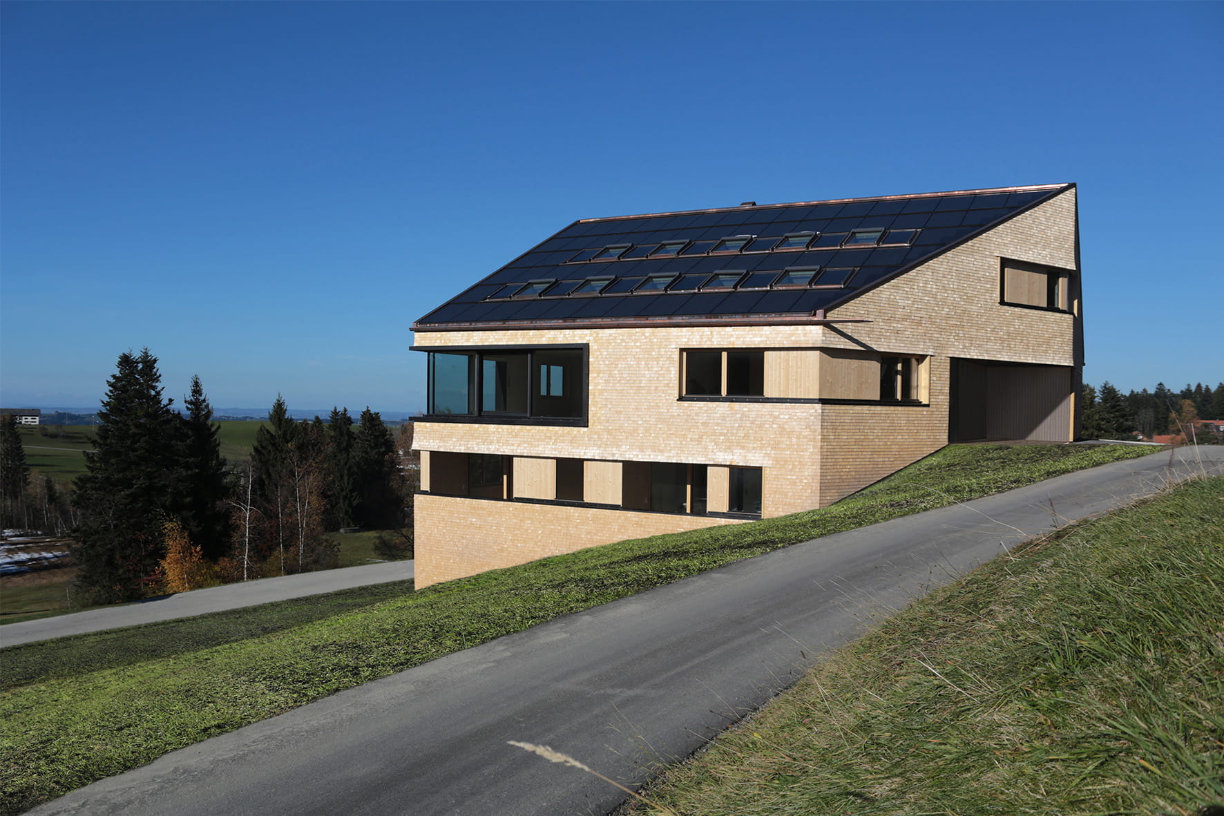 Nachhaltiges modernes Zuhause mit VELUX Dachflächenfenstern an einem grünen Hang unter blauem Himmel.