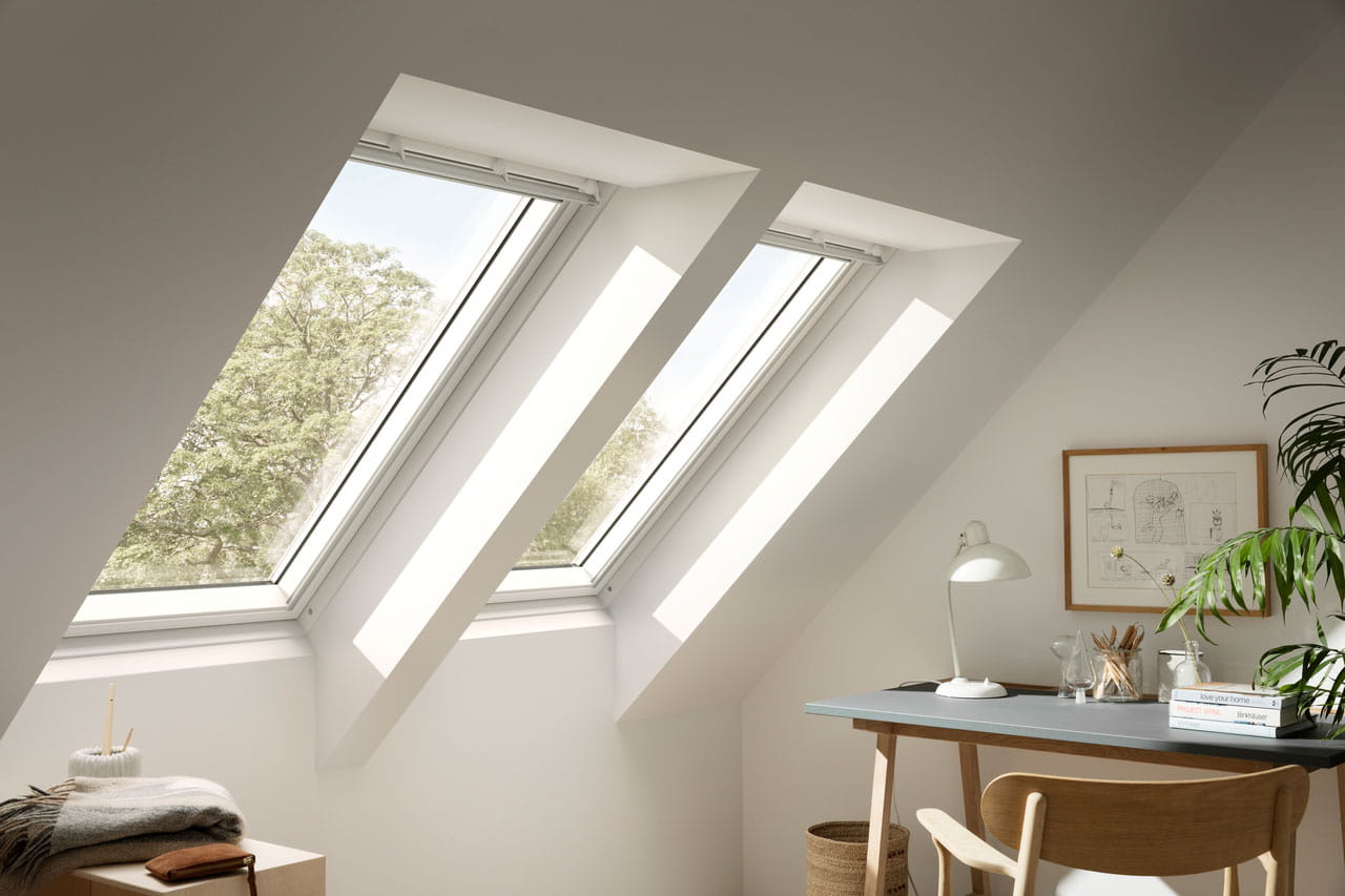 Gemütliches Dachboden-Homeoffice mit natürlichem Licht von VELUX Dachflächenfenstern und einer Aussicht auf Bäume.