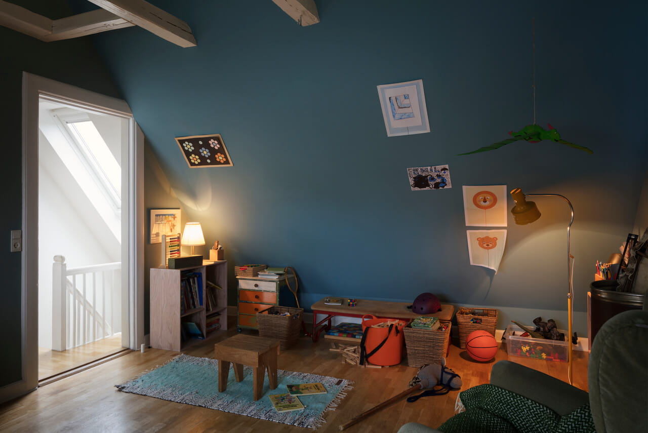 Kinderzimmer mit blauen Wänden, VELUX-Fenster, Spielzeug und hölzernen Möbeln.