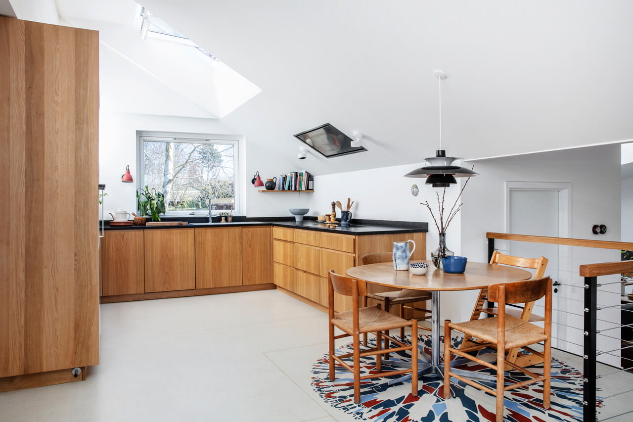 Moderne Küche mit hölzernen Schränken, Esstisch, VELUX Dachflächenfenster und buntem Teppich.