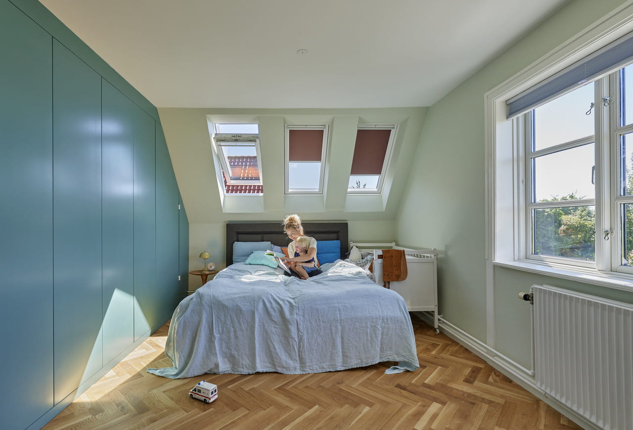 Schlafzimmer im Dachboden mit VELUX Dachflächenfenstern, blauer Bettwäsche und Fischgrätparkett.