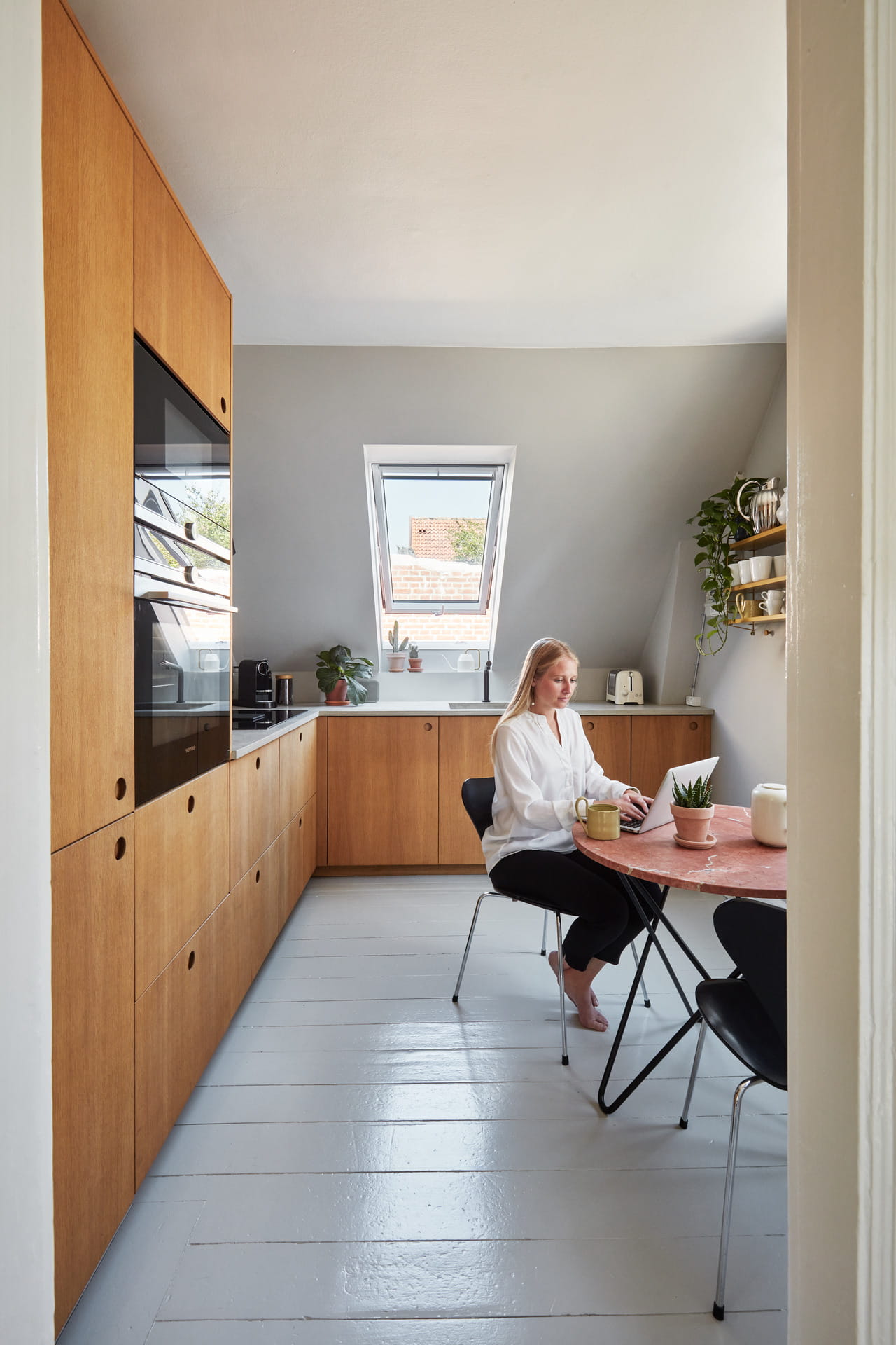 Moderne Küche mit hölzernen Schränken, VELUX-Fenster und Person am Tisch mit Laptop.