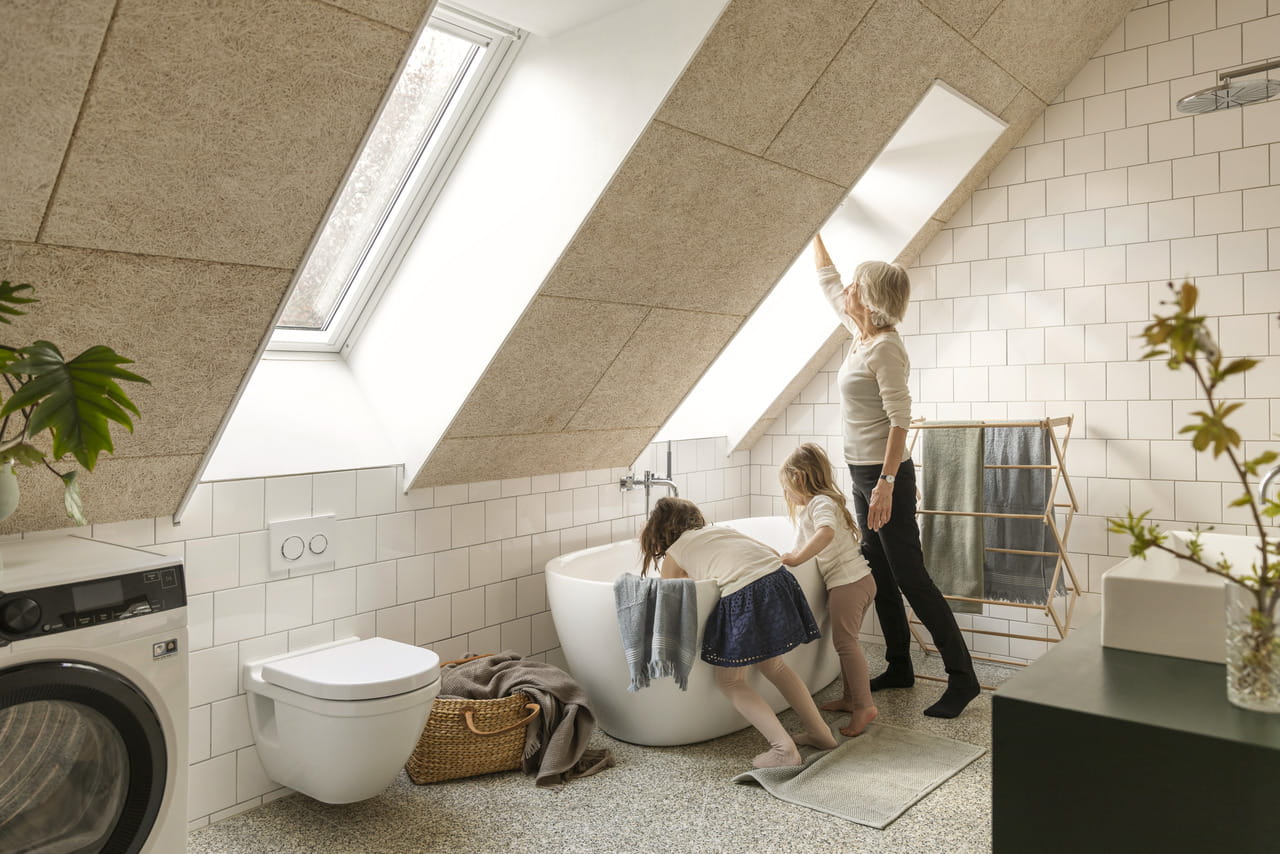 Mutter mit Kindern in einem hellen Badezimmer mit VELUX Dachflächenfenstern und moderner Einrichtung.
