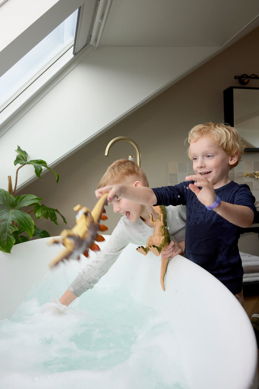 Two kids playing with toy dinosaurs next to the bath tub.
