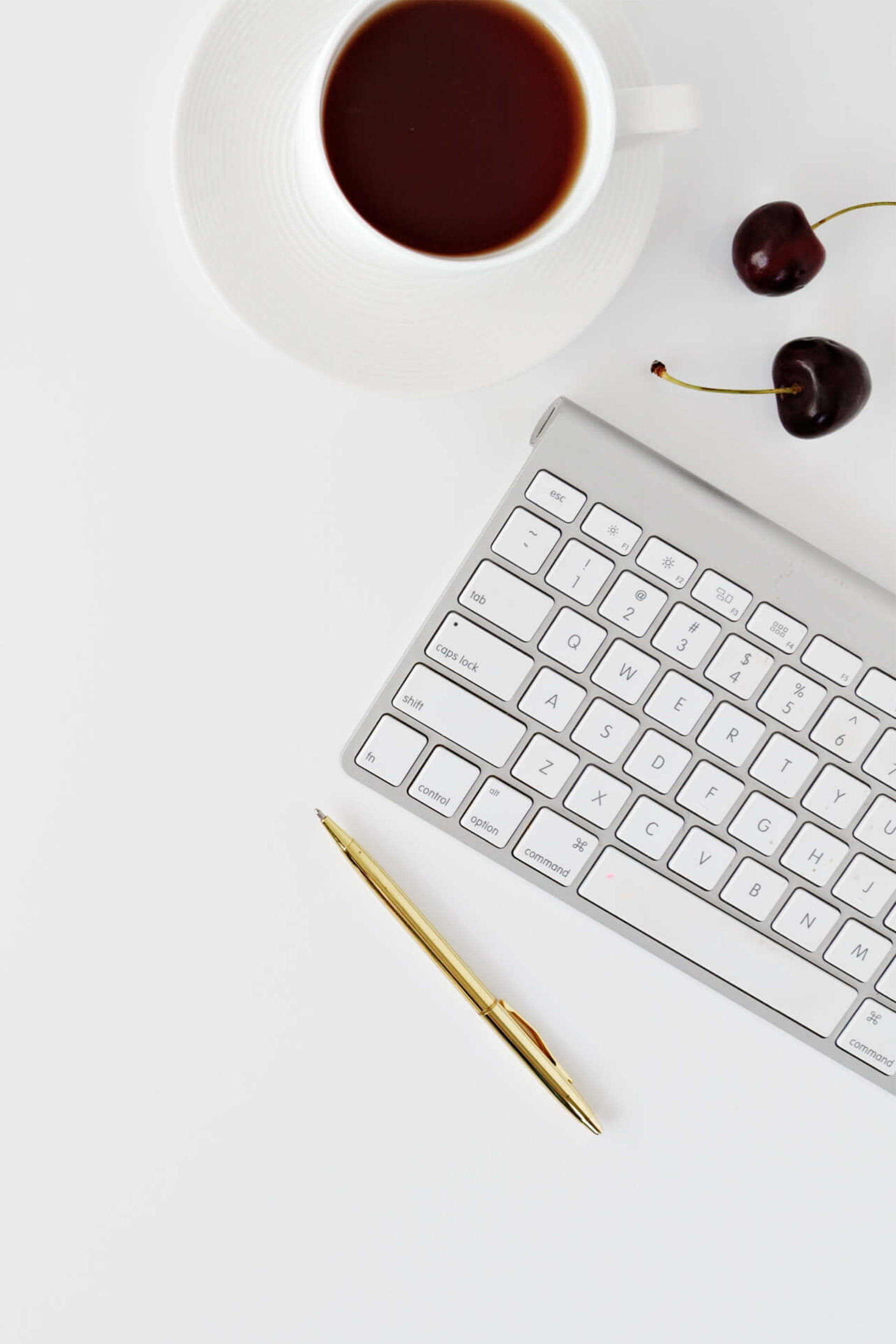 Moderner weißer Schreibtisch mit Tastatur, Kaffee und Kirschen, der Minimalismus zur Schau stellt.