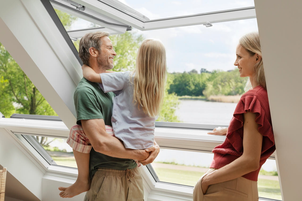 Family in a bright room with a VELUX window overlooking greenery.