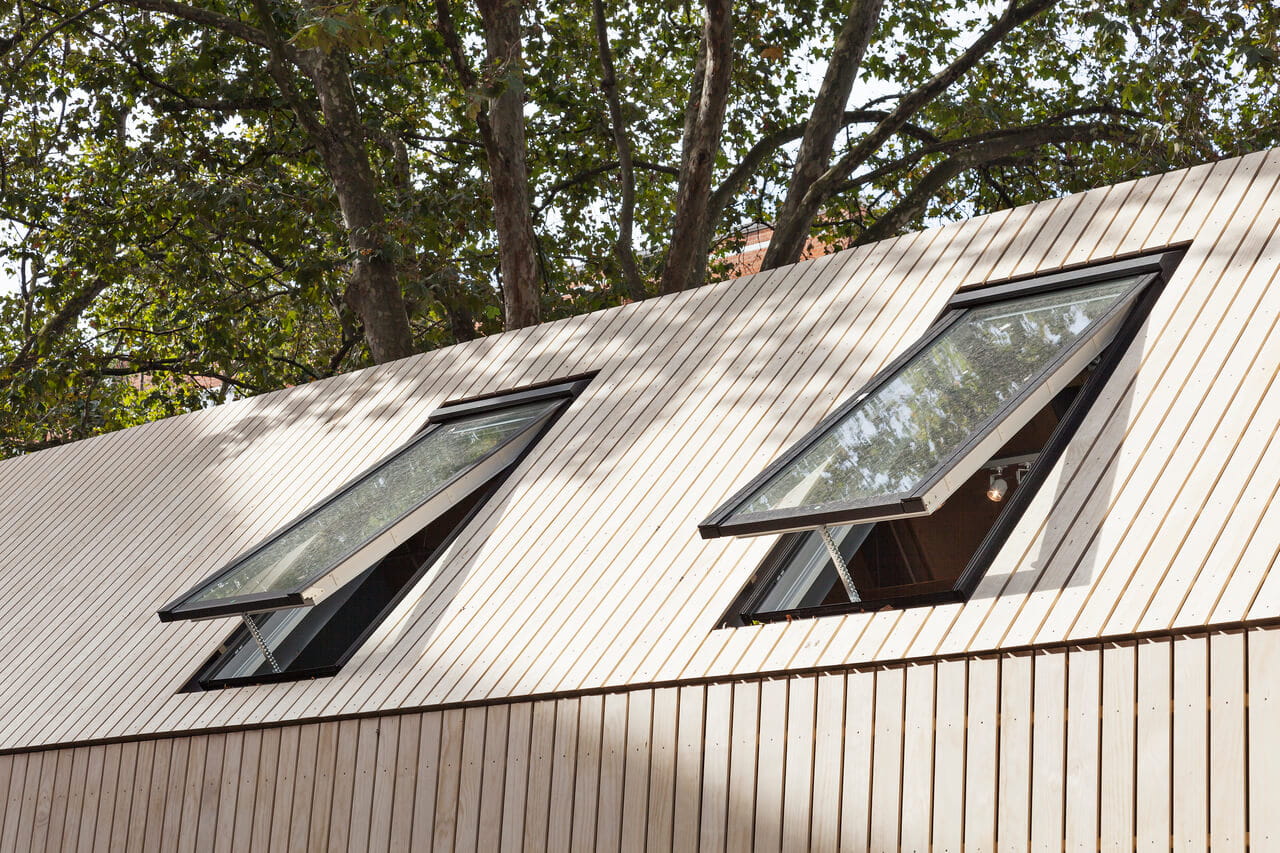 Two VELUX roof windows on a slanted wooden roof amidst green trees.