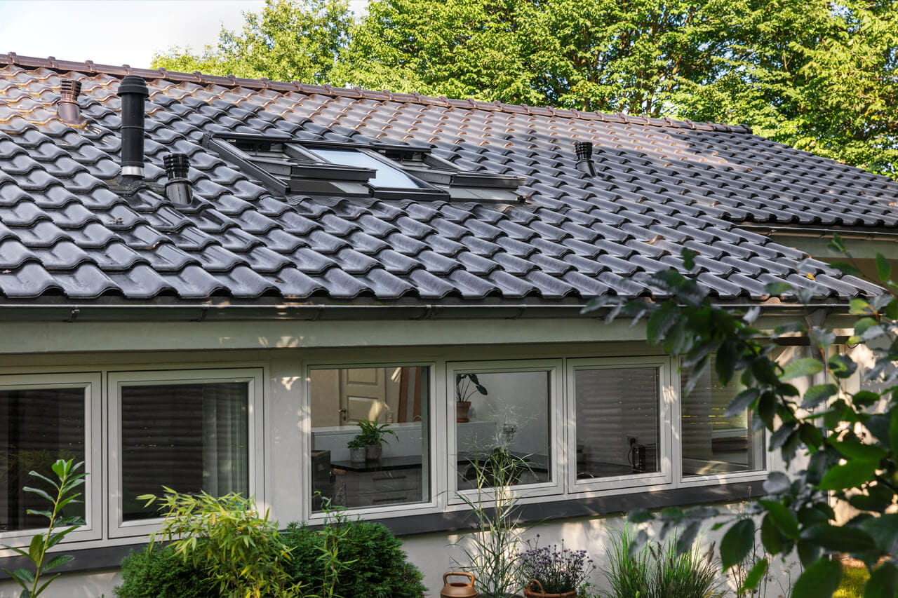 Casa unifamiliar moderna con ventanas de tejado VELUX y tejas oscuras, rodeada de vegetación.