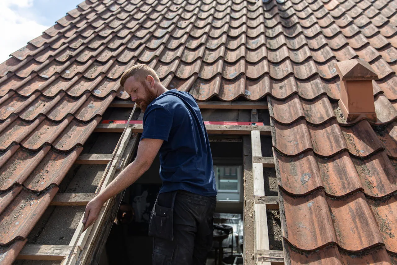 Werknemer die een VELUX dakvenster installeert op een betegeld dak, waardoor de verlichting in huis verbetert.