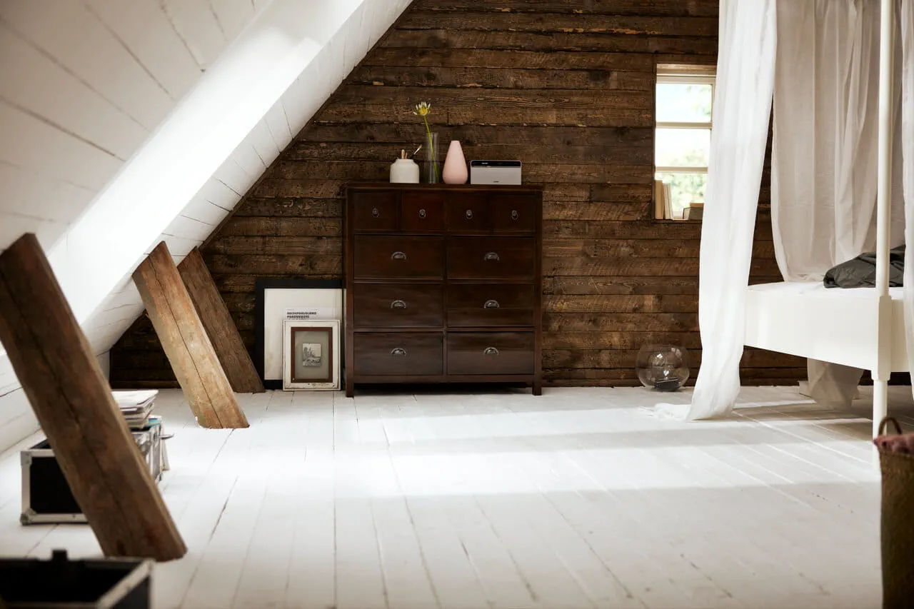 Chambre mansardée confortable avec fenêtre de toit VELUX, murs en bois et sol blanc.