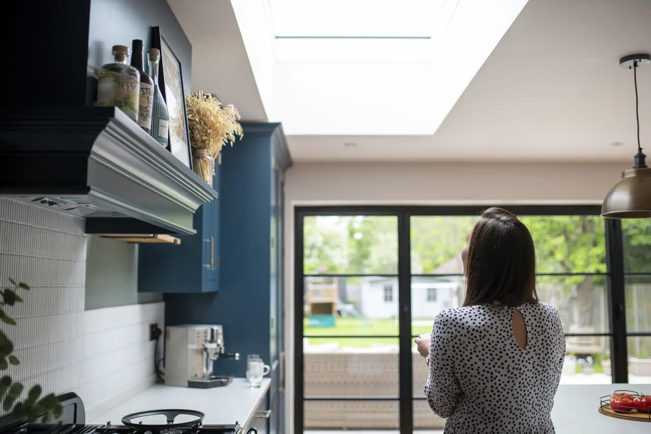 Femme dans une cuisine ensoleillée avec une fenêtre de toit VELUX et une vision du jardin.