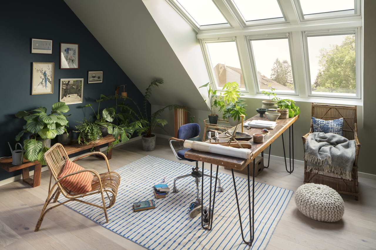 Thuiskantoor op zolder met houten bureau, rotan stoel, planten en VELUX dakvensters.