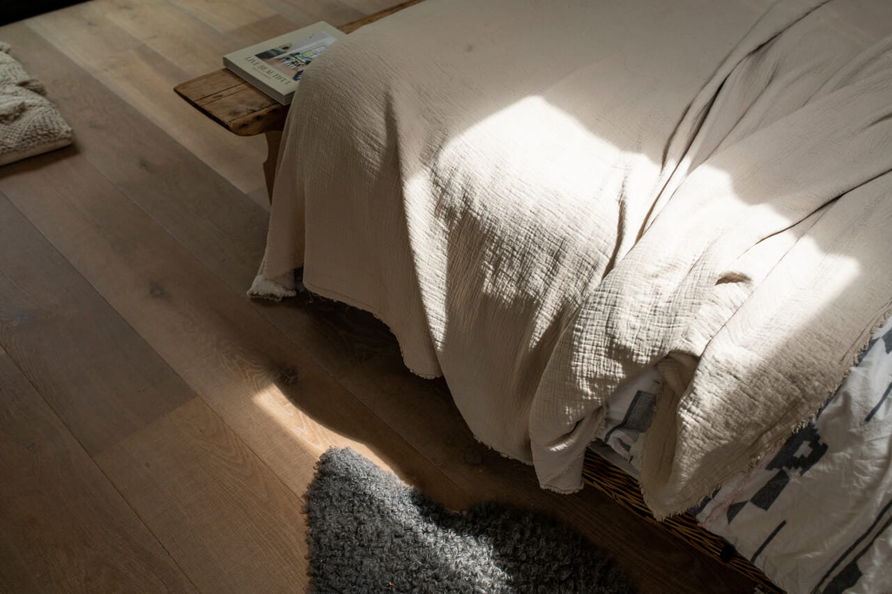 Solljus som strömmar in på en säng med texturerade linnelakan i en lugn sovrumsinredning.