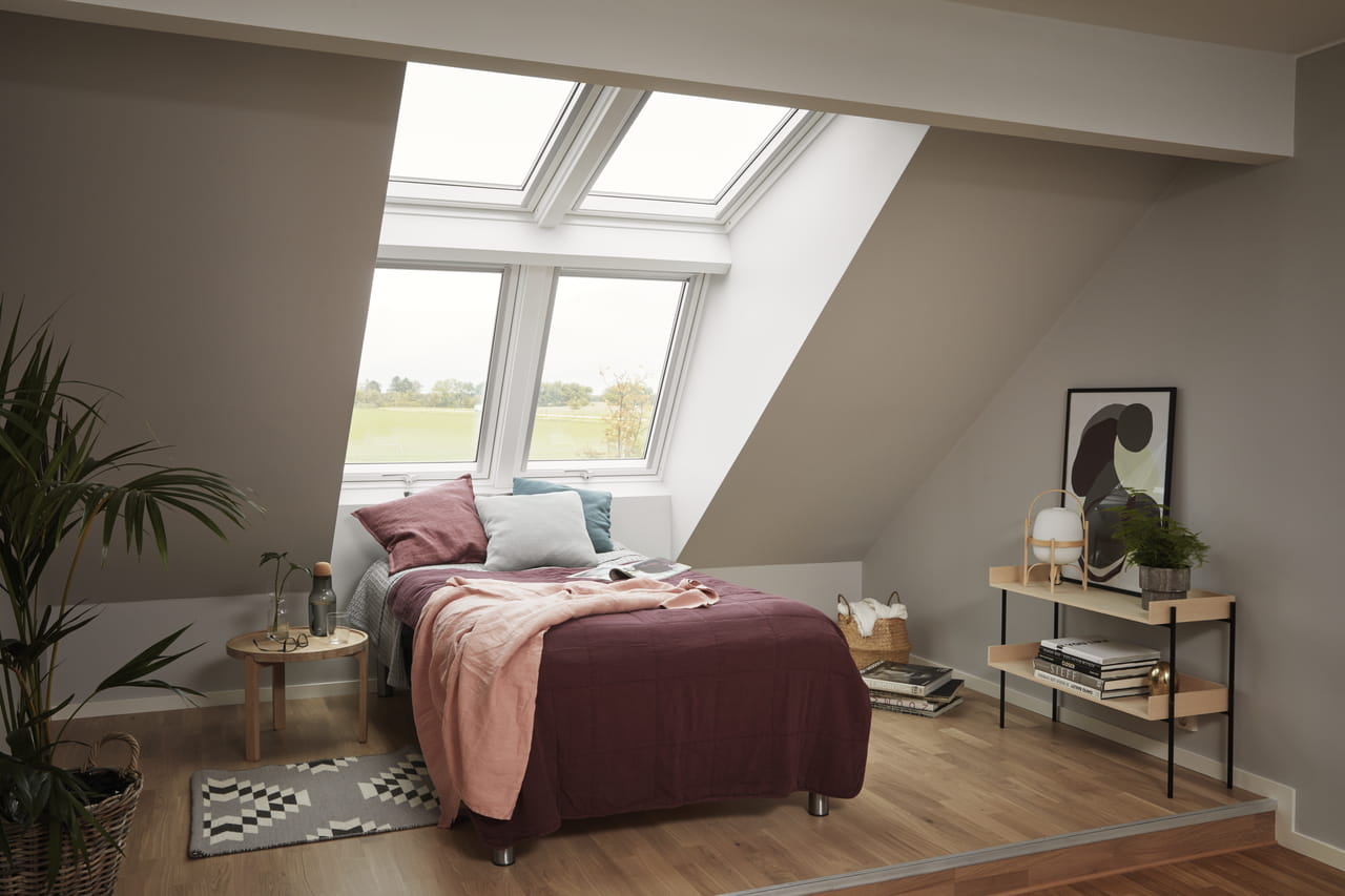 Slaapkamer op zolder met bed, moderne inrichting en VELUX dakvensters die natuurlijk licht binnenlaten.