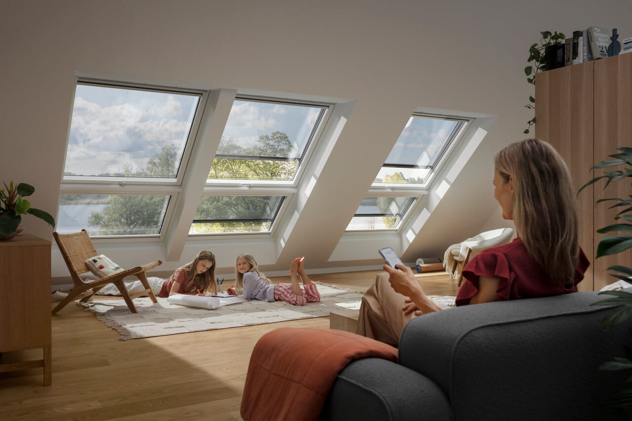 Salle familiale de grenier avec des fenêtres de toit VELUX, un coin salon et des enfants jouant sur le tapis.