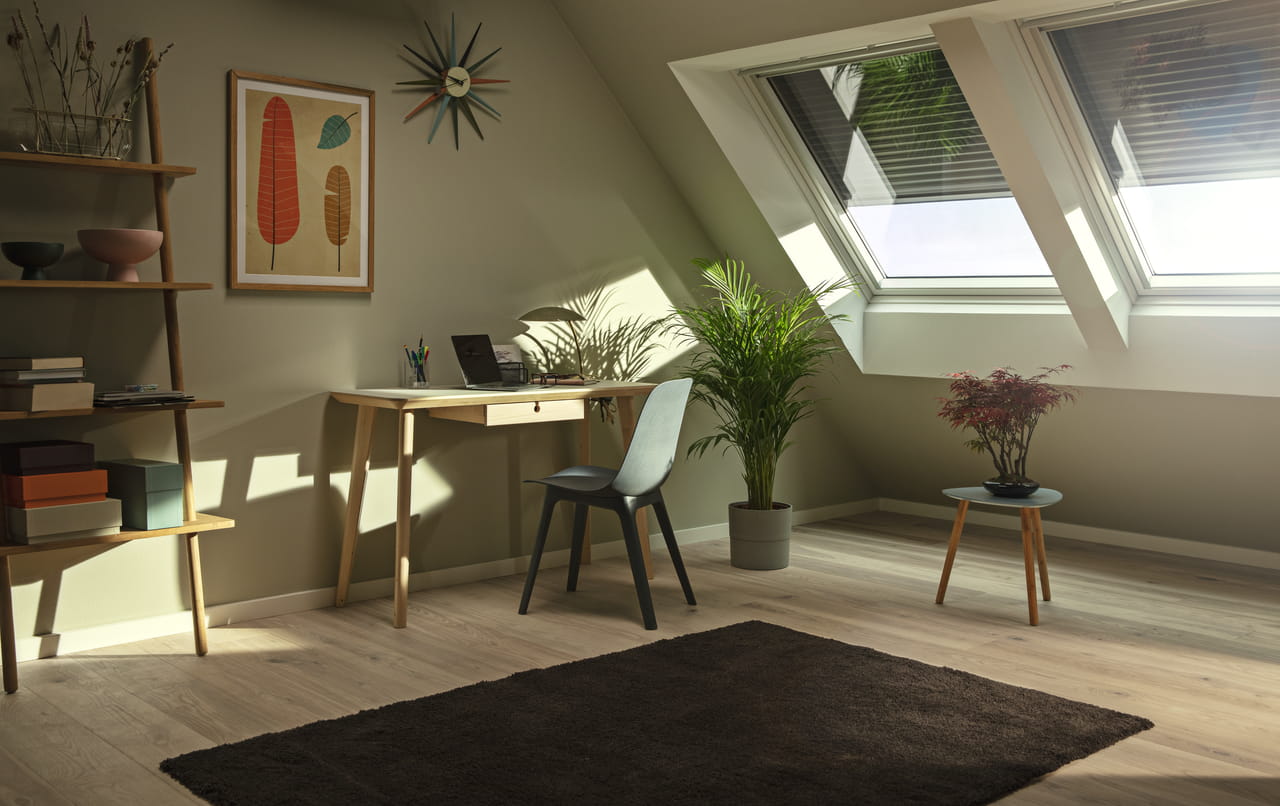 Hyggeligt loftsrum hjemmekontor med naturligt lys fra VELUX ovenlysvinduer og indendørs planter.