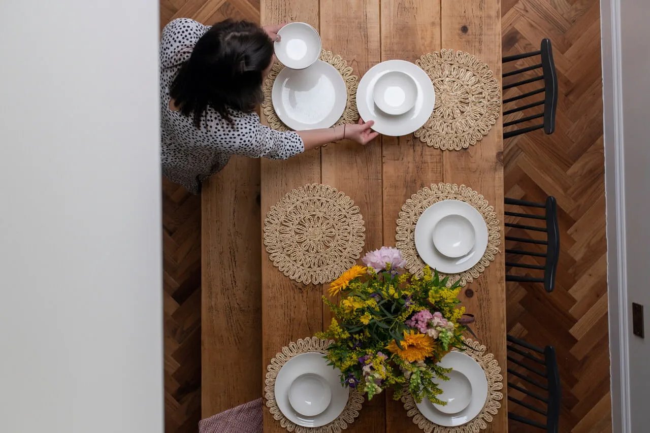 Vue aérienne de la table à manger avec des assiettes blanches, des sets de table tissés et une pièce maîtresse colorée.