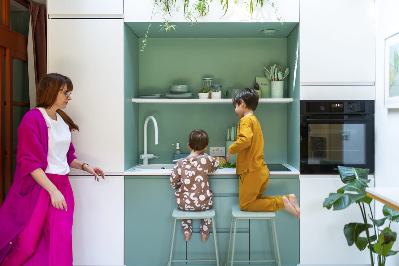 Moderne keuken met spelende kinderen, omgeven door groen en hedendaagse apparaten.