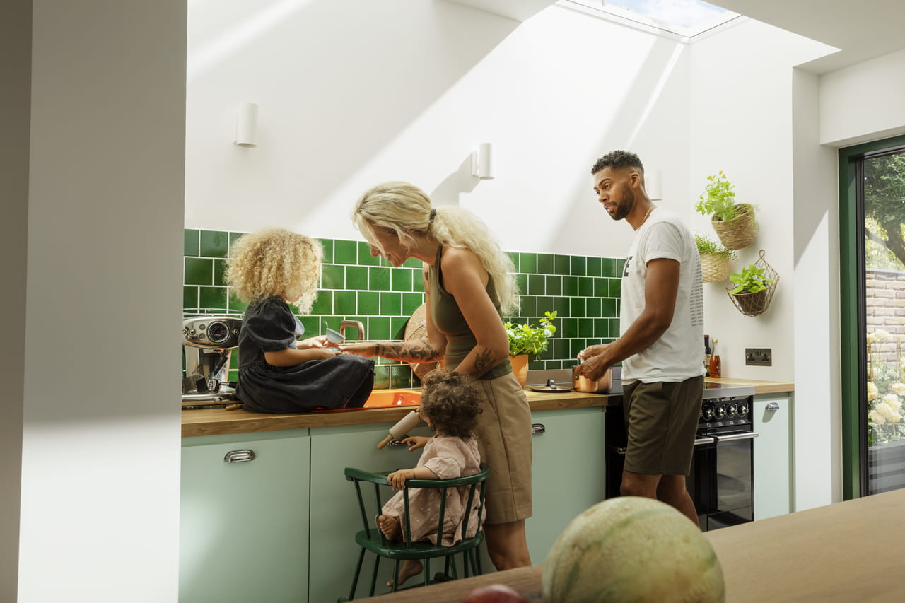 Zonovergoten moderne keuken met familie aan het koken, VELUX dakvenster erboven.