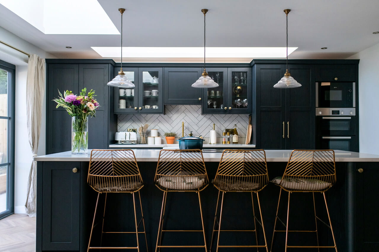 Cocina moderna con gabinetes negros, encimera blanca, ventana de tejado VELUX y luces colgantes.