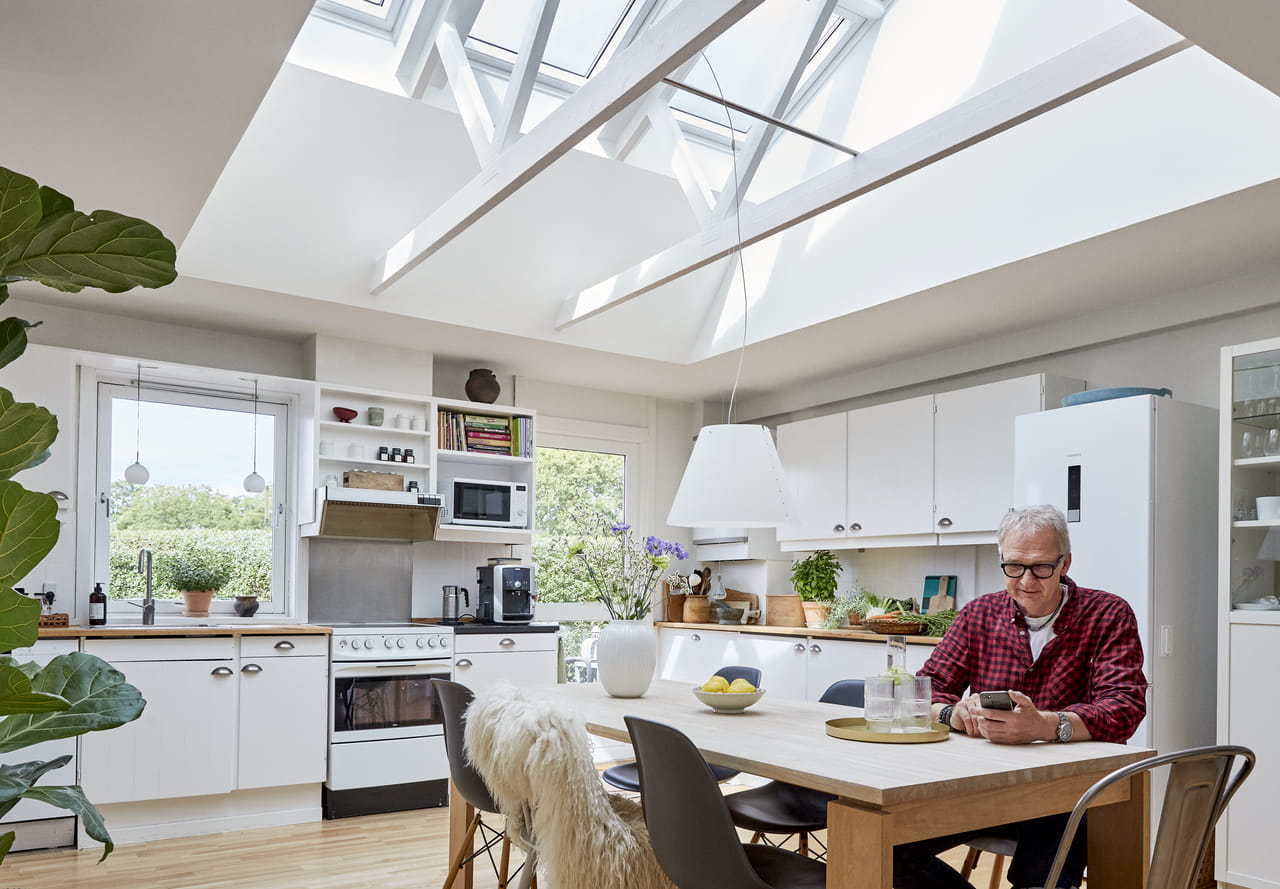 Modernt kök med naturligt ljus från VELUX takfönster, vita skåp och trä- matgrupp.
