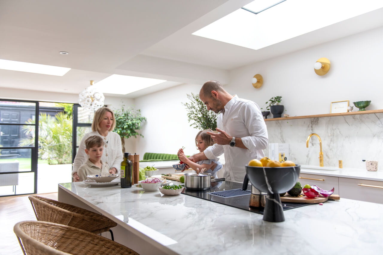 Moderne keuken met VELUX dakvenster, familie kookt, marmeren werkbladen, uitzicht op de tuin.