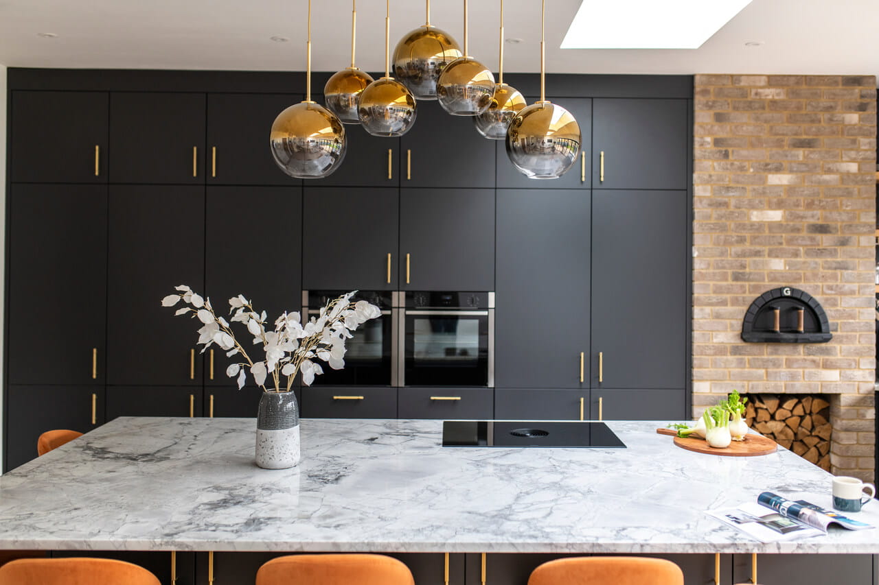 Stylish kitchen with black cupboards, marble worktop, gold lighting, and a VELUX skylight.
