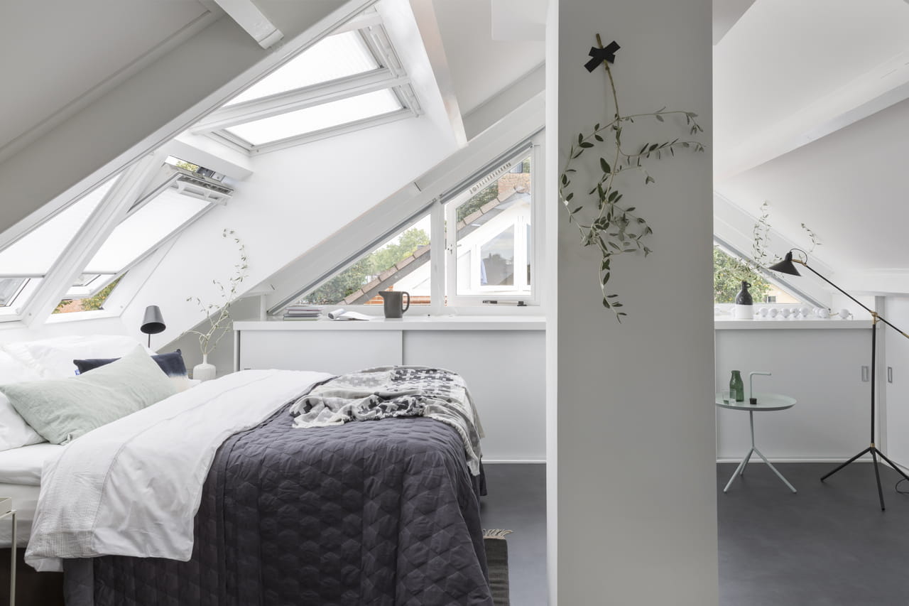 Minimalistische zolder slaapkamer met VELUX dakvensters en moderne inrichting.