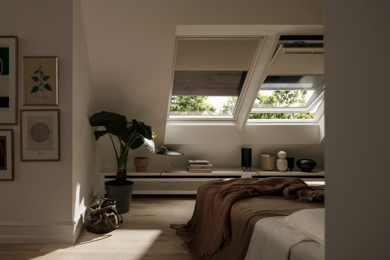 Minimalist bedroom with natural light from VELUX roof windows, cozy bed, and a desk.