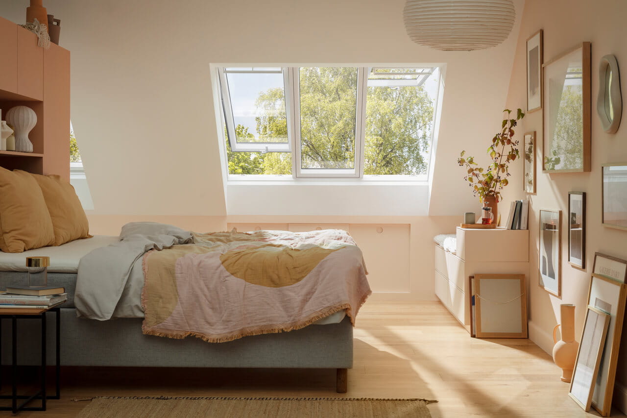 Chambre douillette avec lumière naturelle provenant d'une fenêtre de toit VELUX, décoration chaleureuse et vue sur la verdure.