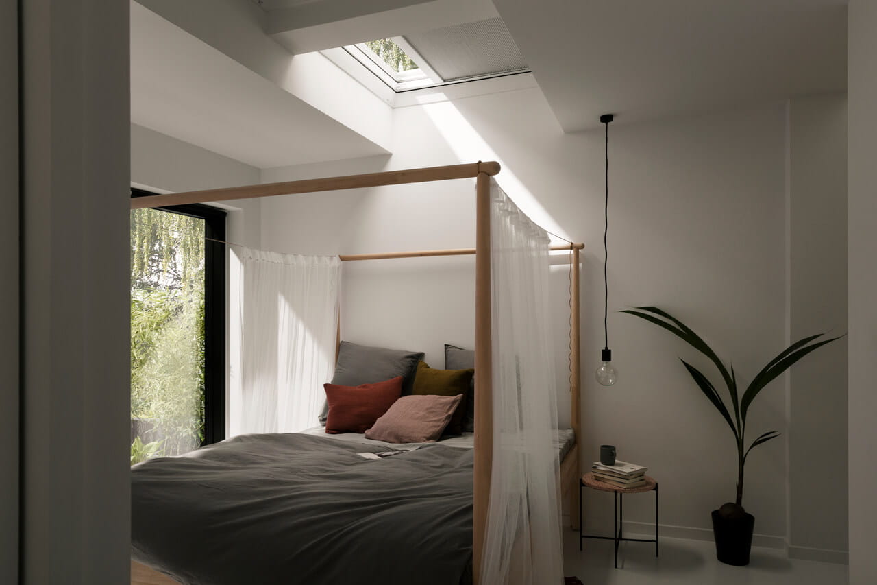 Dormitorio minimalista con ventana de tejado VELUX, cama con dosel y planta de interior.