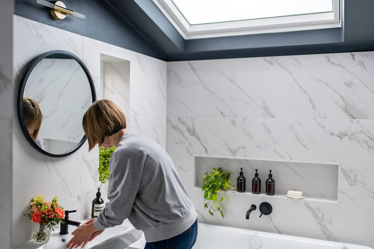 Hedendaagse badkamer met marmeren muren en een VELUX dakvenster, persoon aan de wastafel.