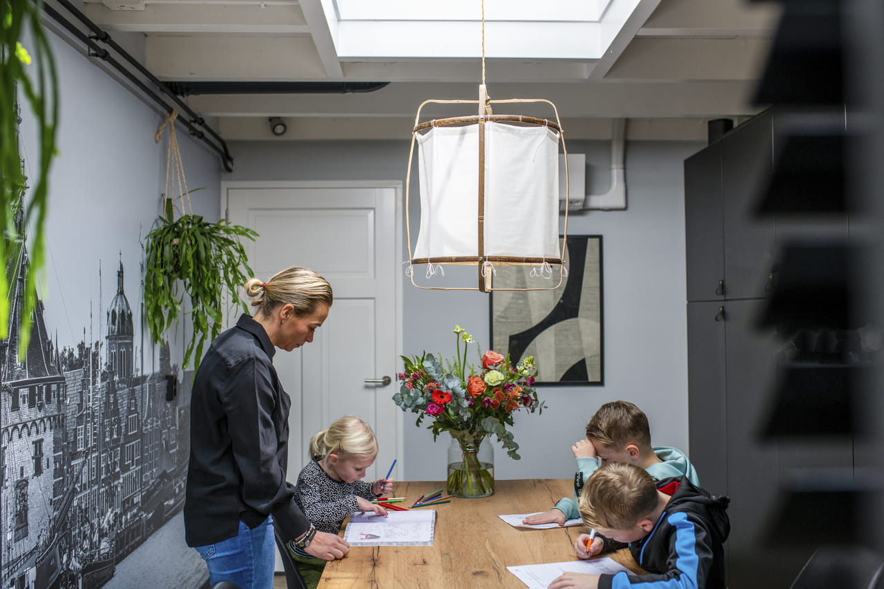 Kinderen die aan een tafel tekenen onder toezicht van een volwassene, in het natuurlijke licht van een VELUX dakvenster.